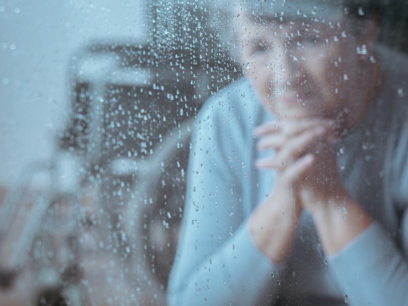 Femeie batrana uitandu-se pe geam la ploaie