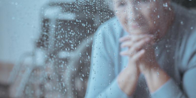 Femeie batrana uitandu-se pe geam la ploaie